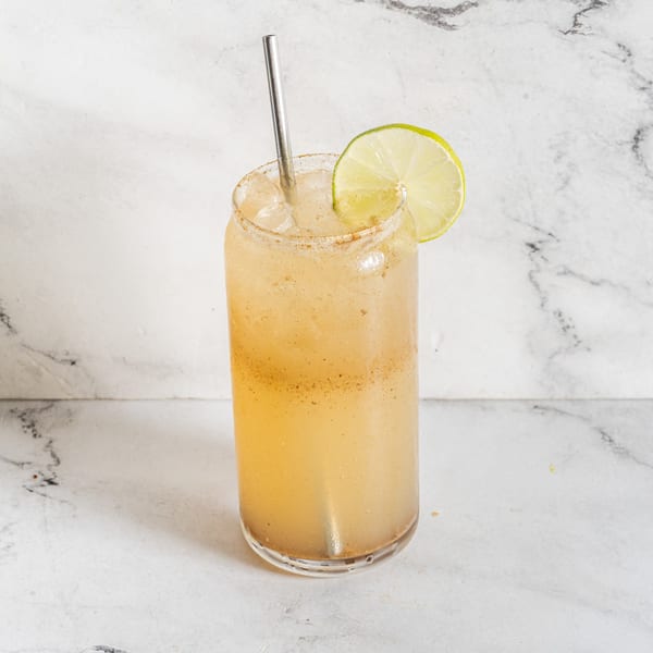 Indian spiced drink with a lime wedge and metal straw in a tall glass.