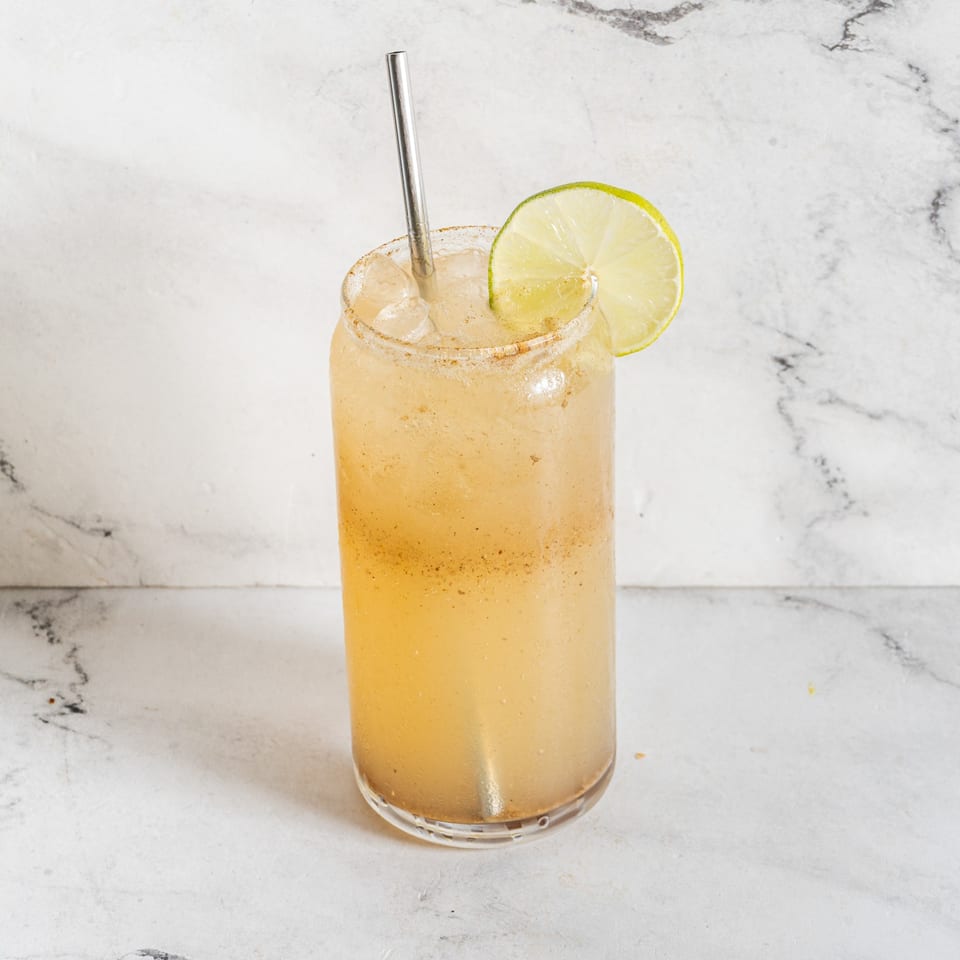Indian spiced drink with a lime wedge and metal straw in a tall glass.