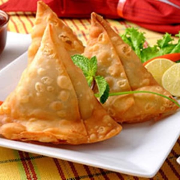 Golden-brown Indian samosas, garnished with mint, lime, and lettuce, served on a white plate.