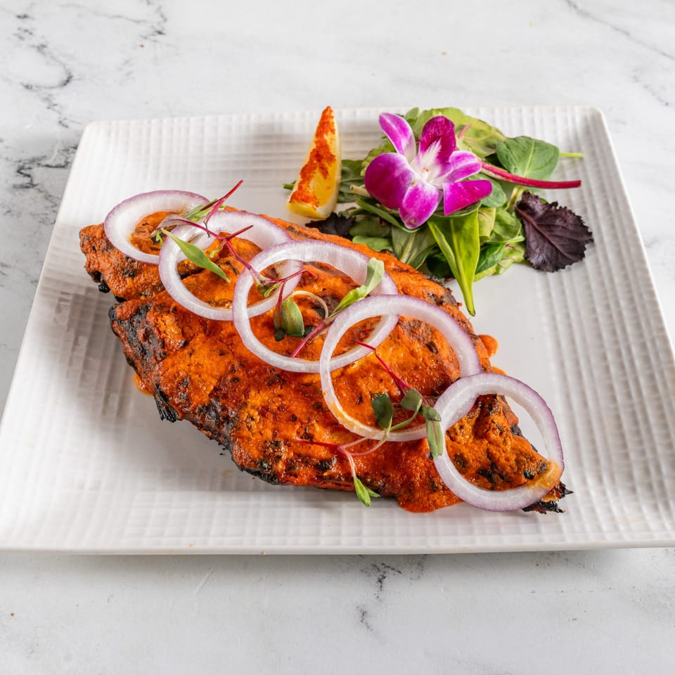 Indian tandoori fish with red onions, microgreens, lemon, and an orchid on a white plate.