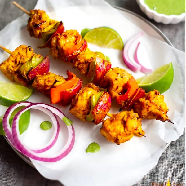 Indian chicken tikka skewers with bell peppers, onions, and lime wedges on a white plate.