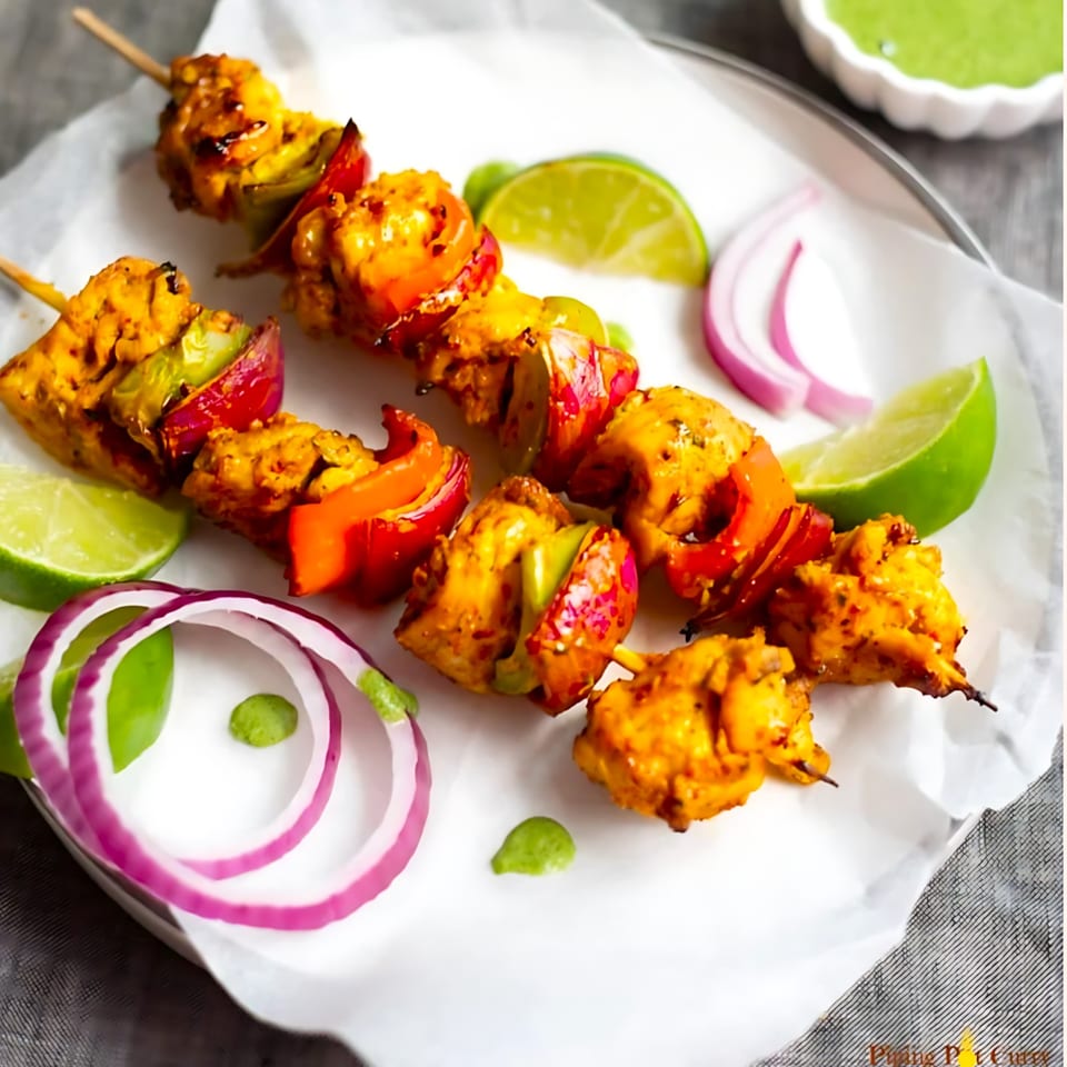 Indian chicken tikka skewers with bell peppers, onions, and lime wedges on a white plate.