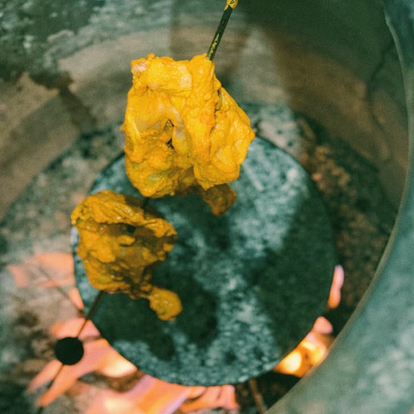 Marinated chicken pieces on skewers cooking inside a tandoor oven with visible flames.