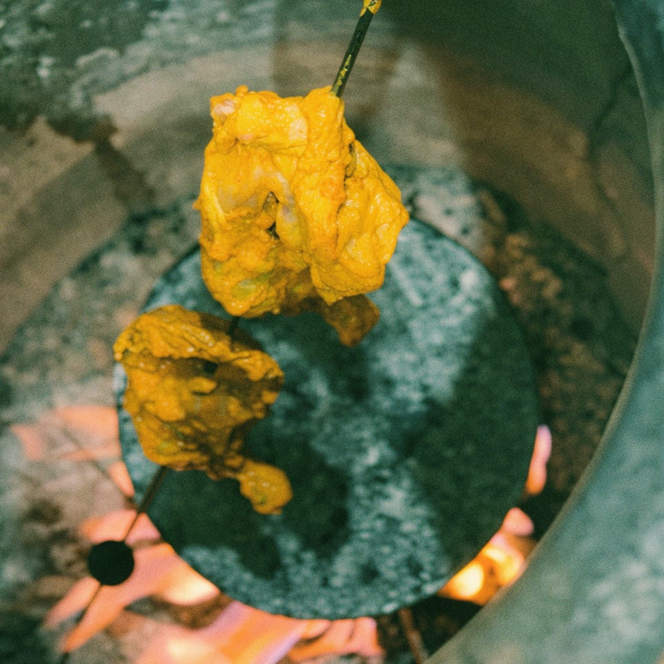 Marinated chicken pieces on skewers cooking inside a tandoor oven with visible flames.