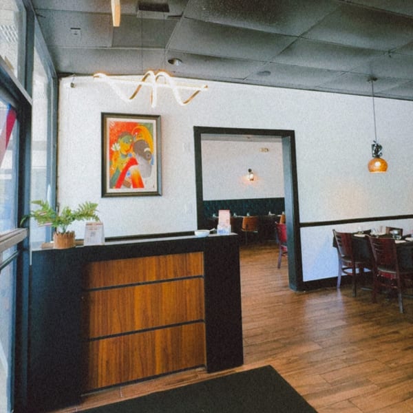 Restaurant entrance with a wooden host stand, modern art, and a glimpse into the dining area.
