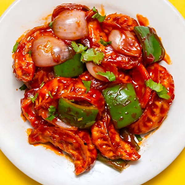 Indian chili momos with red sauce, green bell peppers, and onions on a white plate.