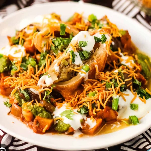 Indian samosa chaat with yogurt, green chutney, and crispy sev on a white plate.