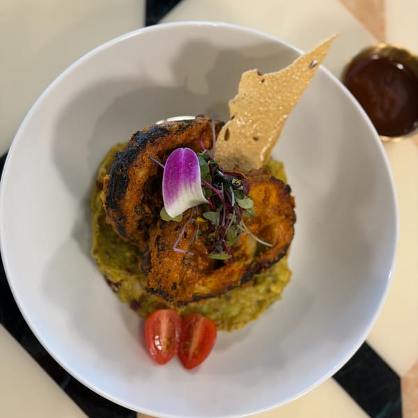 Indian dish with grilled chicken, green puree, cherry tomatoes, and a purple flower garnish.