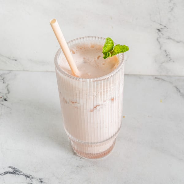 A glass of creamy Indian lassi with a straw and mint garnish on a marble surface.