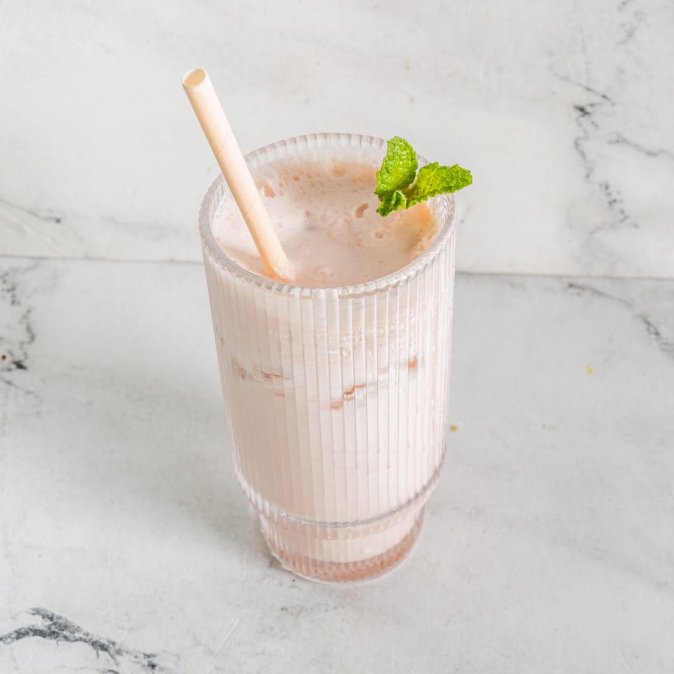 A glass of creamy Indian lassi with a straw and mint garnish on a marble surface.