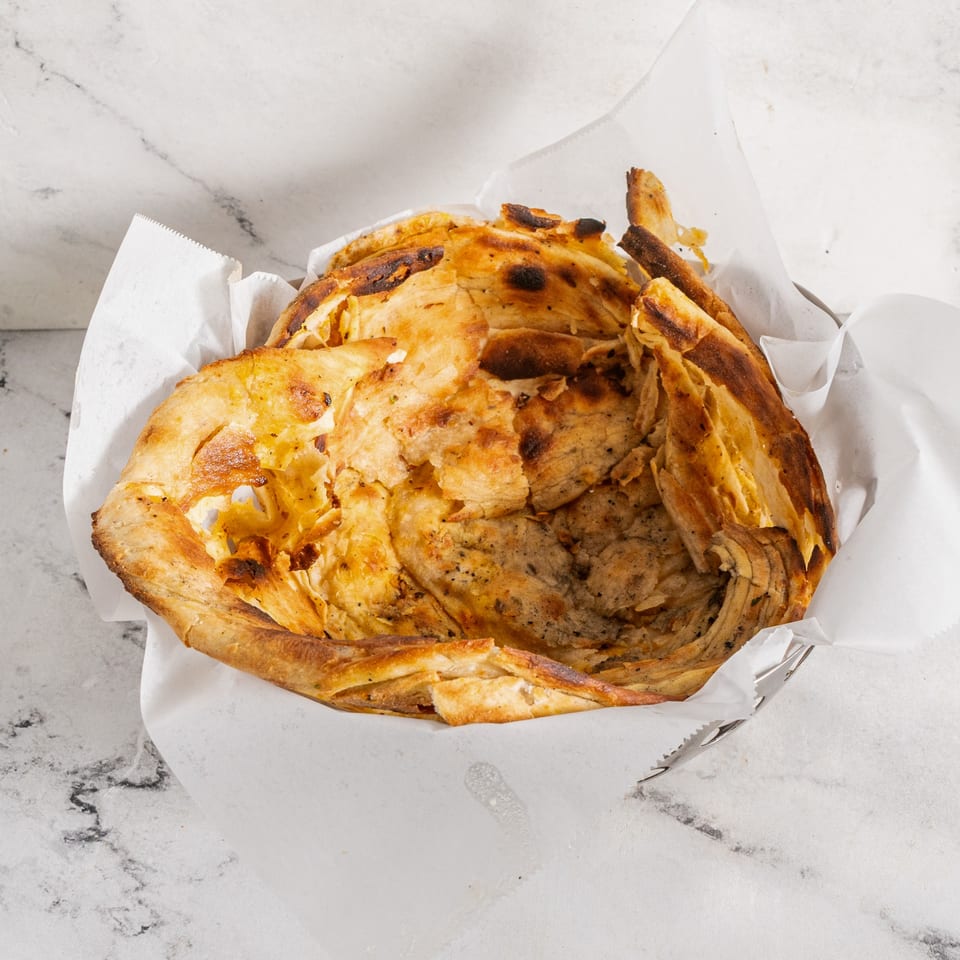 Close-up of golden-brown, flaky Indian paratha bread in a white paper-lined basket.