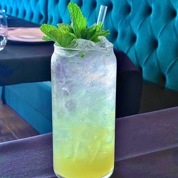 A refreshing green cocktail with crushed ice, fresh mint, and a straw on a dark table.