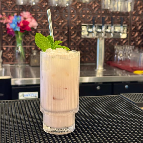 A light pink cocktail with ice, mint, and a metal straw on a bar mat.